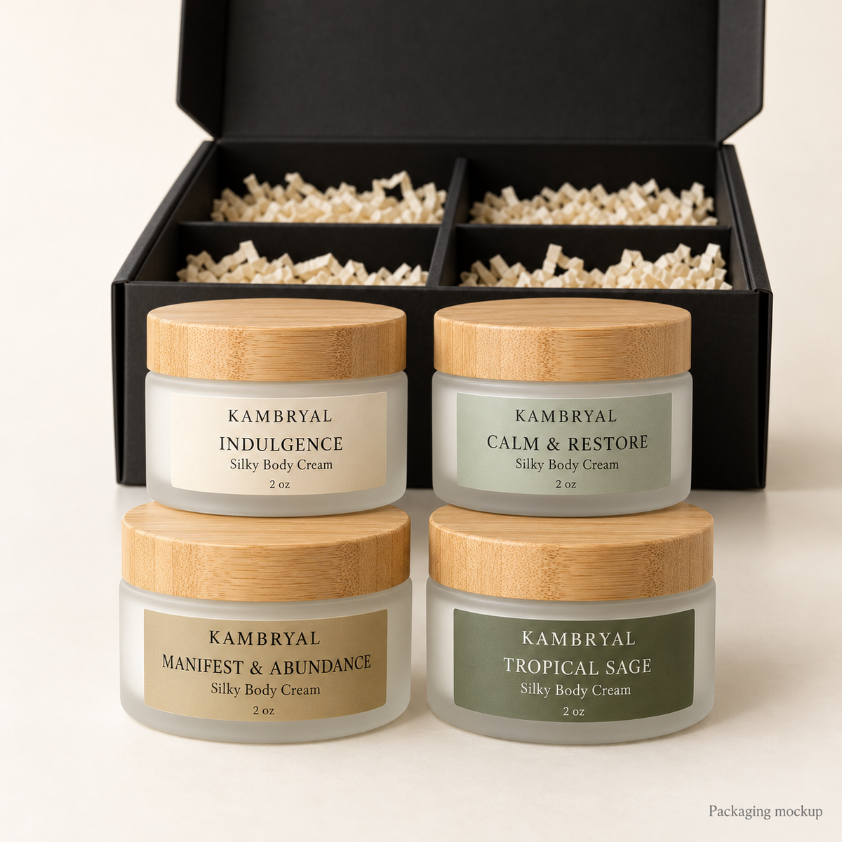 Packaging mockup of KAMBRYAL four-pack sampler: four frosted 2 oz jars with bamboo lids in Indulgence, Calm & Restore, Manifest & Abundance, and Tropical Sage, with black gift box.